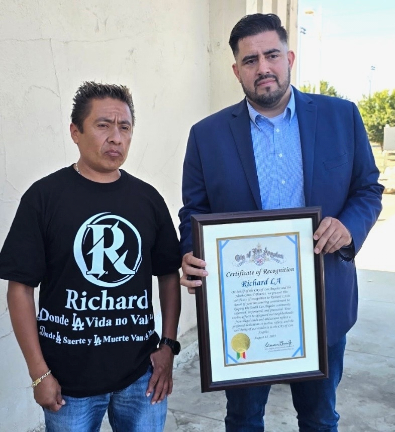FILE - In this photo provided by the office of Los Angeles City Councilmember Curren Price, Carlitos Ricardo Parias, left receives a certificate of recognition from Jose Ugarte, chief of staff for Los Angeles City Councilmember Curren Price in Los Angeles, Aug. 2025. (Office of Los Angeles City Councilmember Curren Price via AP)