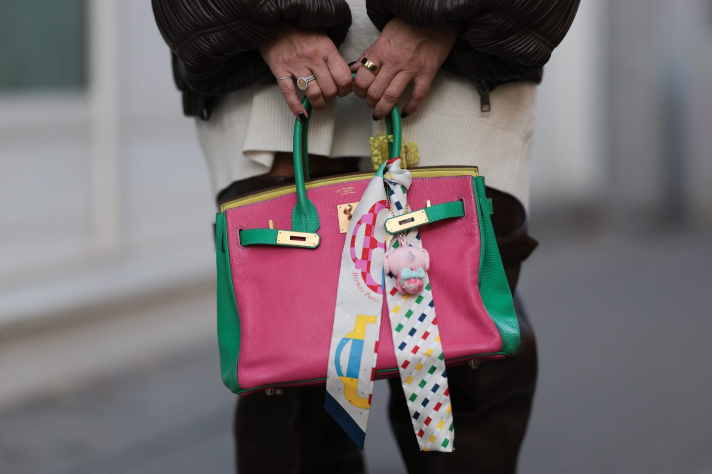 A woman holds a colorful pink and green Birkin bag in front of her legs.