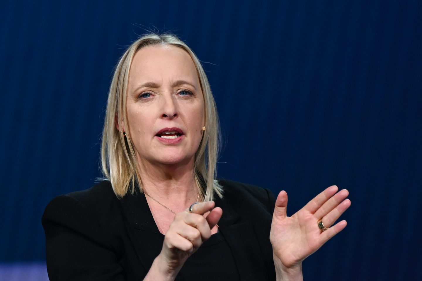 Julie Sweet, in front of a navy blue background, points with one hand.