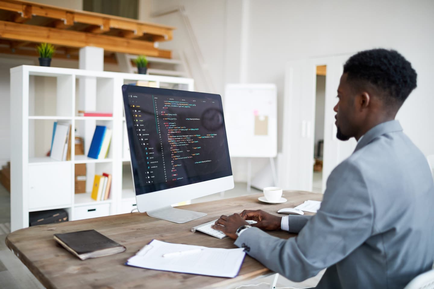 Young elegant software developer in formalwear sitting by desk in front of computer screen while decoding data