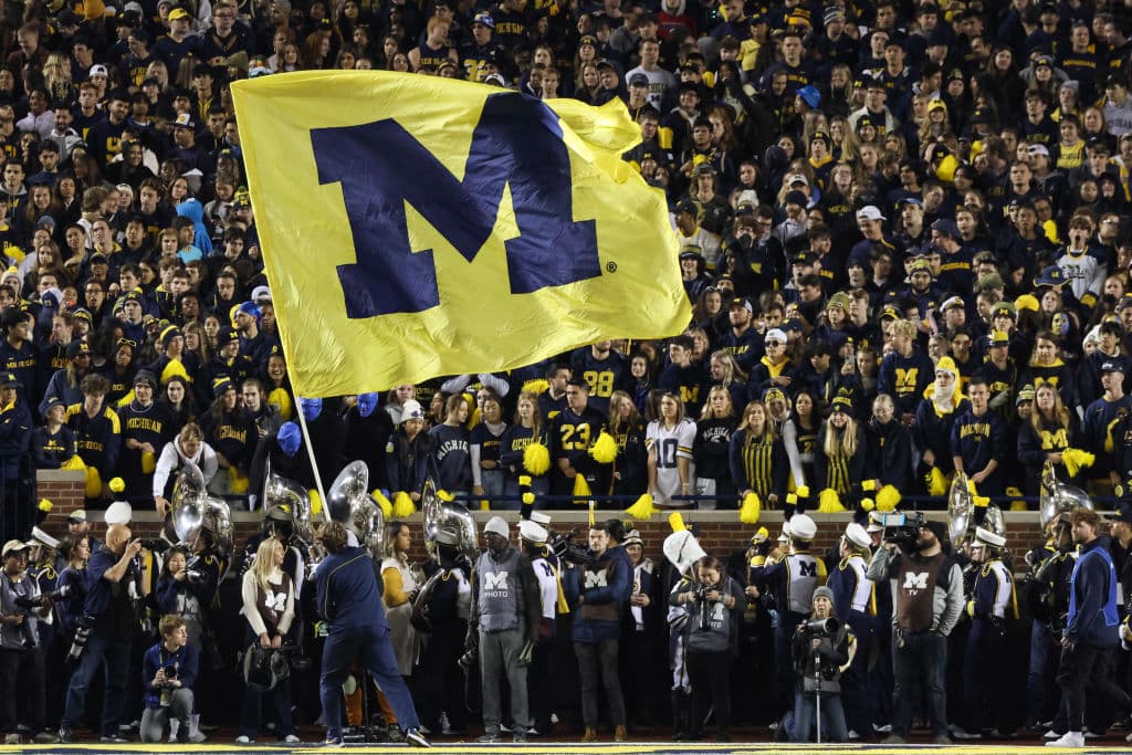 A Michigan cheerleader waves a large flag with the Michigan logo on it during a college football game between the Michigan State Spartans and the Michigan Wolverines, as seen in October 2022 at Michigan Stadium in Ann Arbor, Michigan. (Photo by Scott W. Grau—Icon Sportswire/Getty Images)