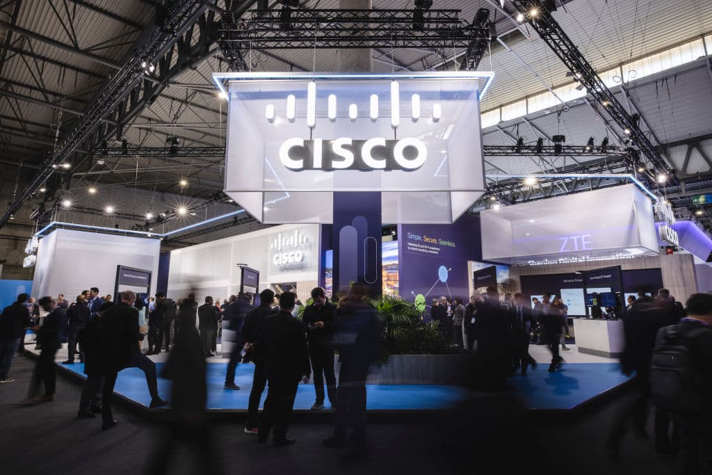 People walk in front of the Cisco booth during the Mobile World Congress 2023 at Fira Barcelona, as seen March 2023 in Barcelona, Spain. (Photo by Cesc Maymo/Getty Images)