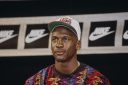 A man with a colorful sweater and "USA" ball cap sits in front of a background with the Nike logo