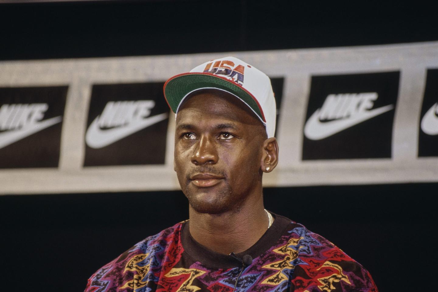 A man with a colorful sweater and "USA" ball cap sits in front of a background with the Nike logo