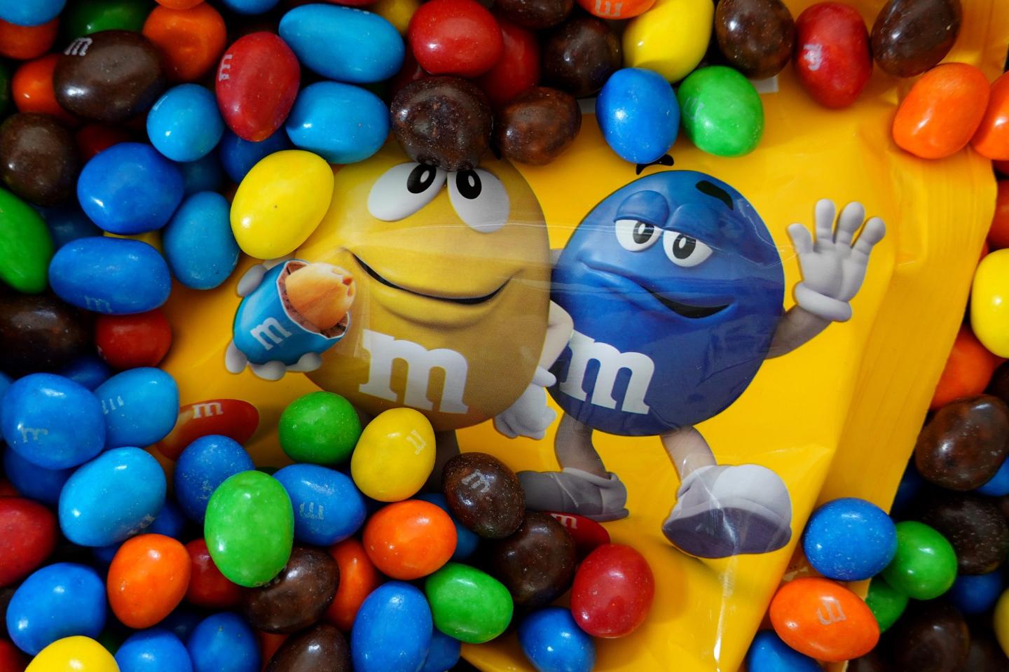 Blue, brown, orange, yellow, and red M&M candies are spread around an M&M bag