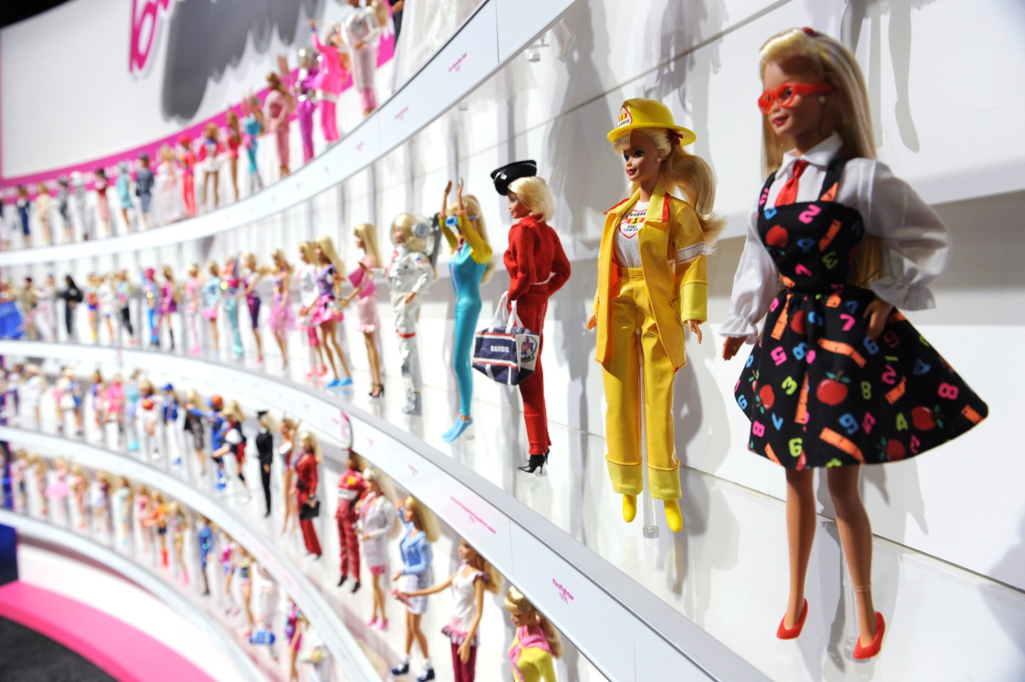 A woman photographs a wall of Barbie dol