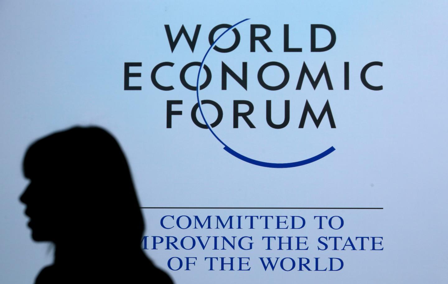 A delegate is silhouetted as she passes by a sign for WEF in Davos