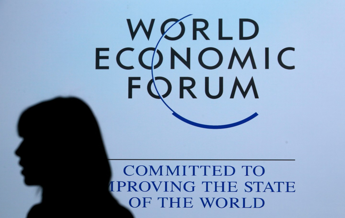 A delegate is silhouetted as she passes by a sign for WEF in Davos