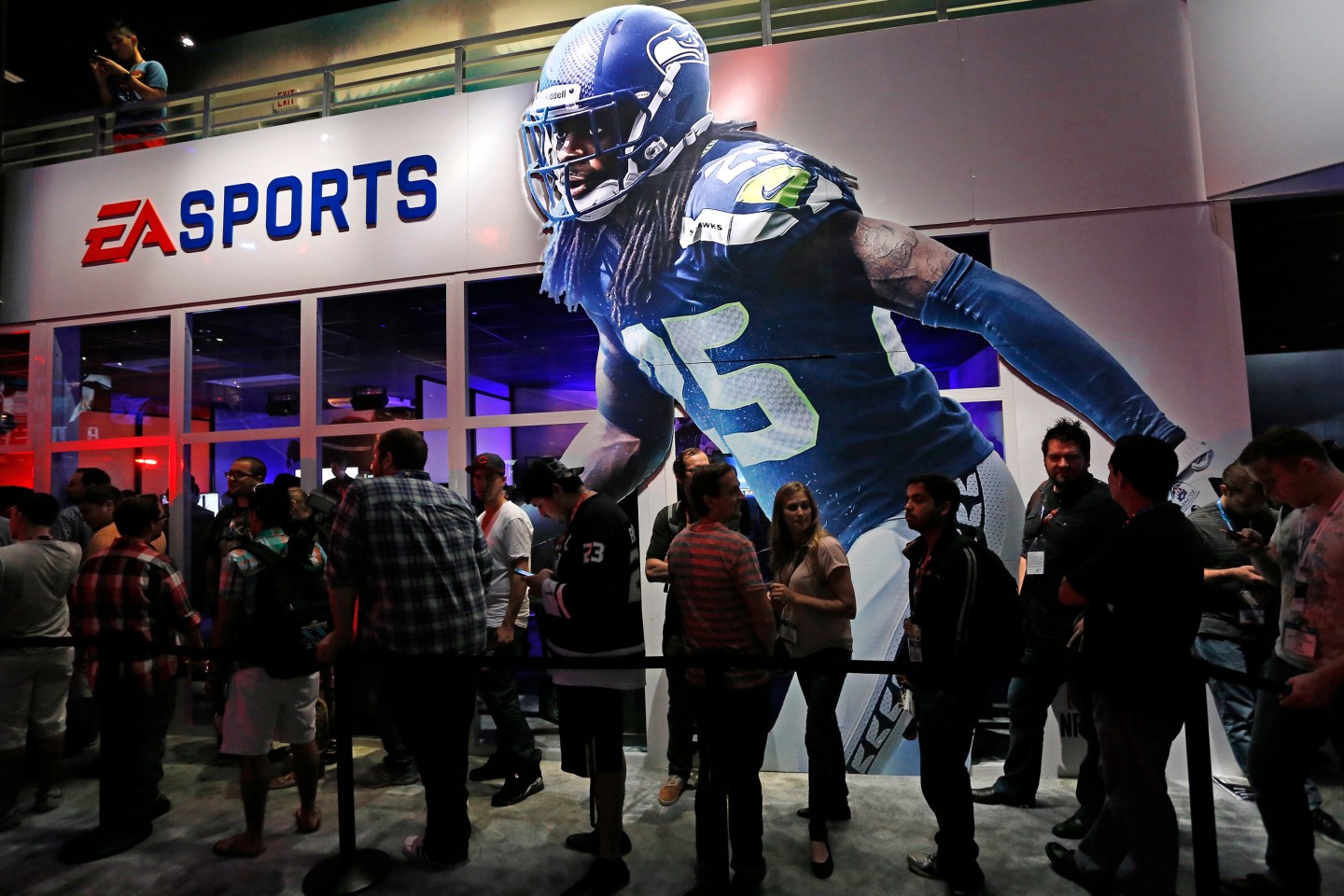 People wait in-line under "Madden NFL 15" billboard with an image of NFL player Sherman at the Electronic Arts booth during the 2014 Electronic Entertainment Expo, known as E3, in Los Angeles