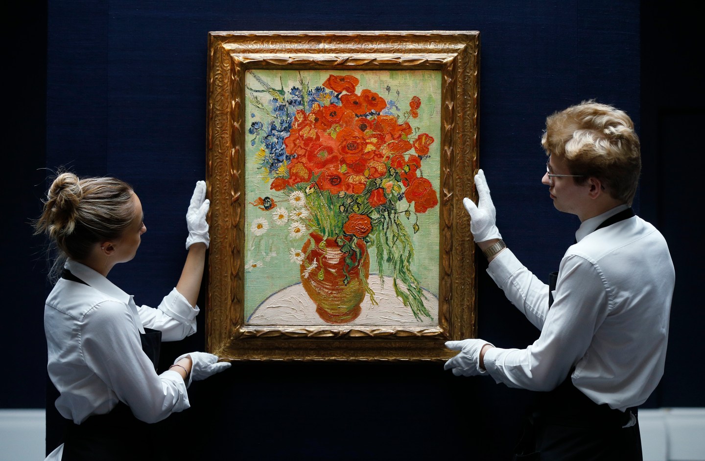 Two staff members pose in a gallery with "Still Life, Vase with Daisies, and Poppies" by Vincent Van Gogh from 1890 at Sotheby's auction house in London