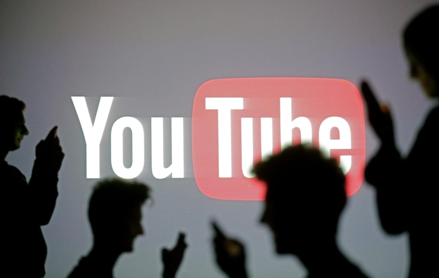 People pose with mobile devices in front of projection of Youtube logo in this picture illustration taken in Zenica