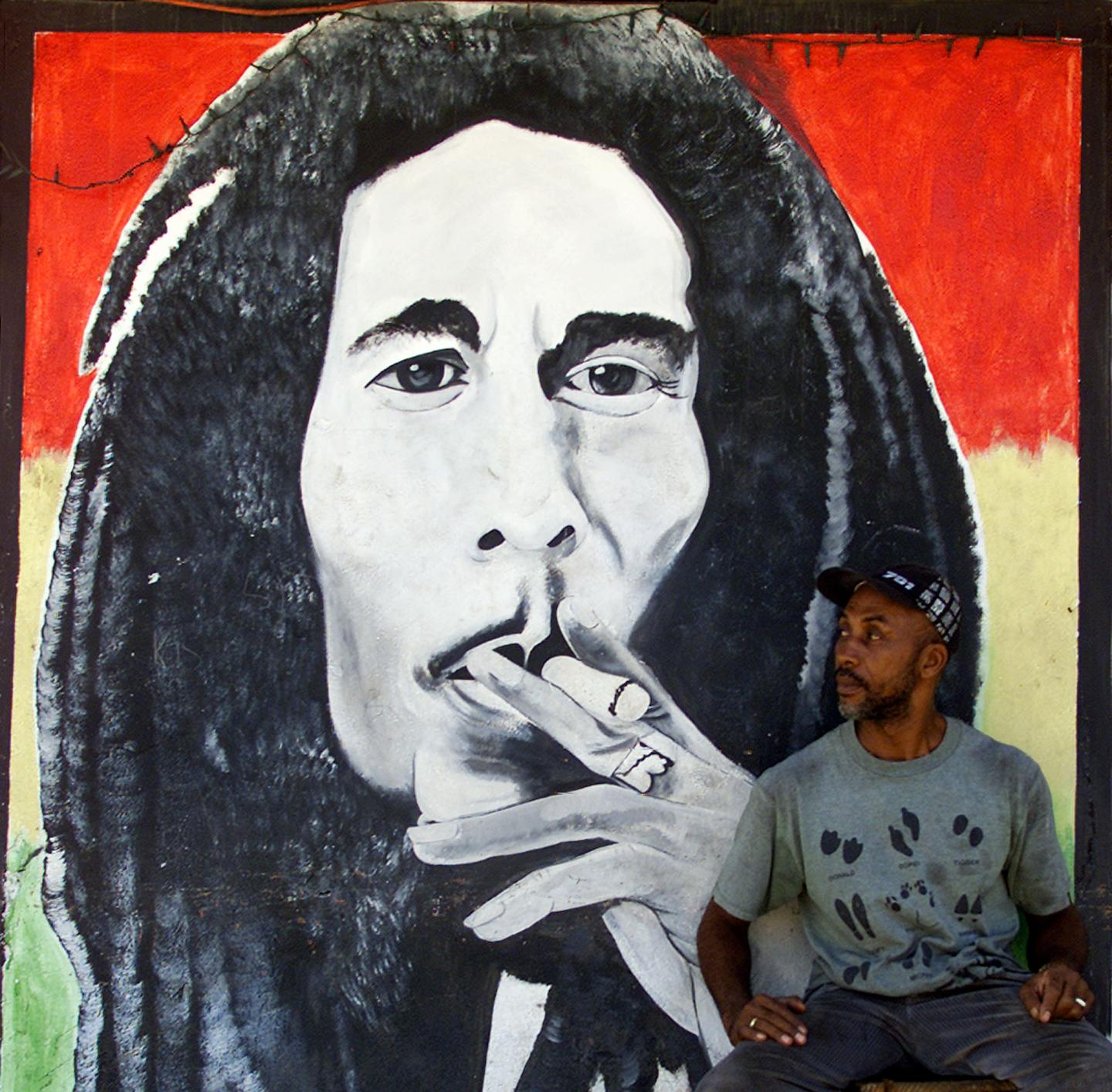 A MAN SITS BY A MURAL OF JAMAICAN REGGAE MASTER BOB MARLEY IN KINGSTON.