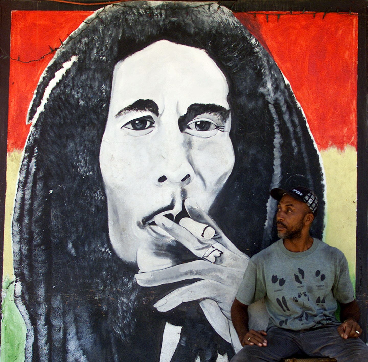 A MAN SITS BY A MURAL OF JAMAICAN REGGAE MASTER BOB MARLEY IN KINGSTON.
