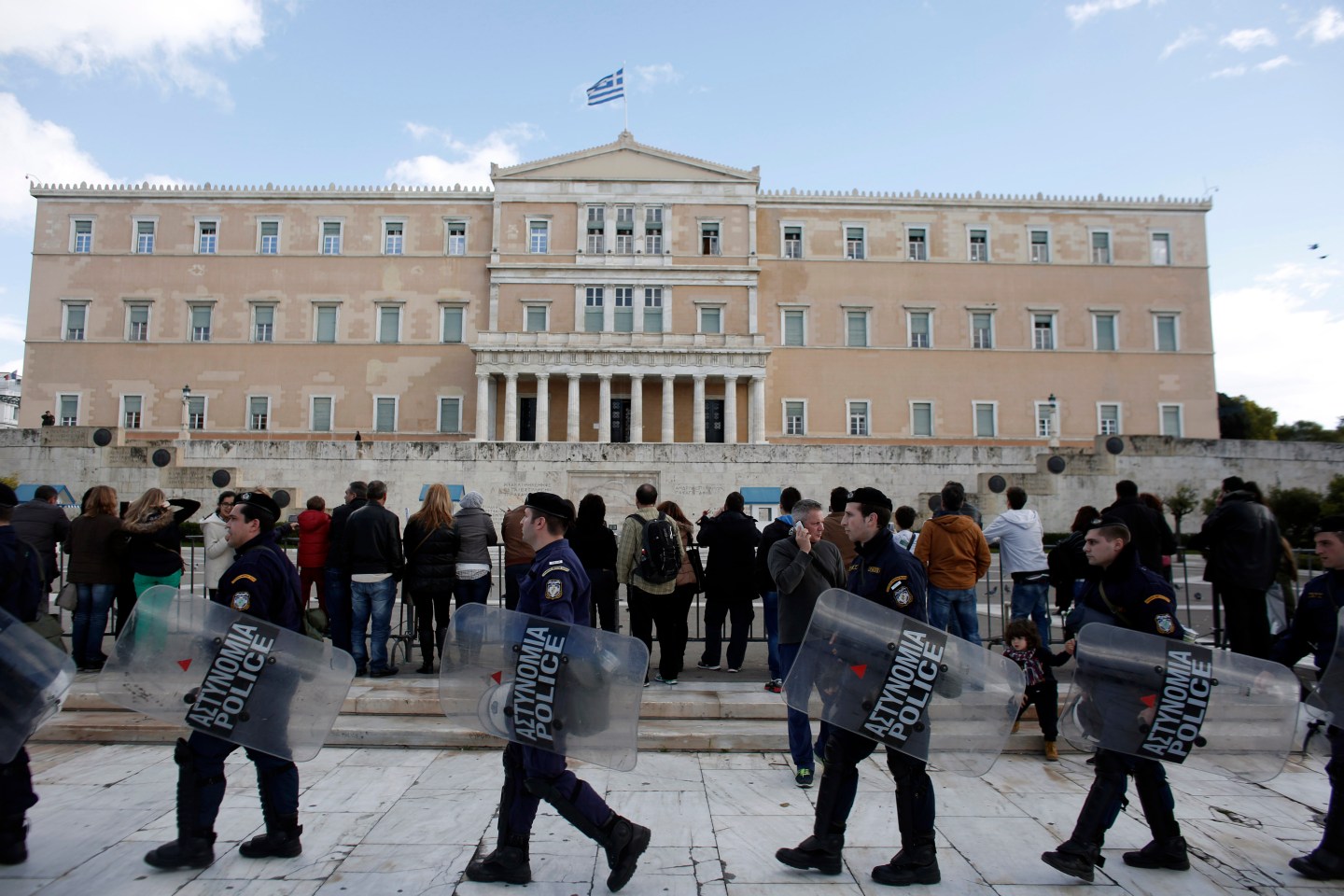 Riot police carry shields past tourists outside the parliament following a final vote by lawmakers for a new Greek president in Athens, Greece, on Monday, Dec. 29, 2014. Greece faces snap elections next month after Prime Minister Antonis Samaras failed in his third and final attempt to persuade parliament to back his candidate for head of state. Photographer: Kostas Tsironis/Bloomberg