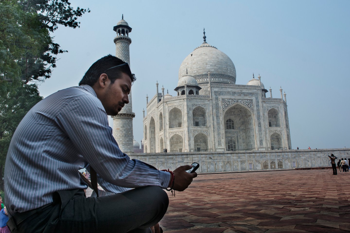 A man checks his cell phone in front of the Taj Mahal. The