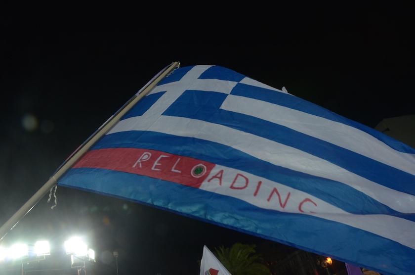 A SYRIZA supporter holds a Greek flag with the word '
