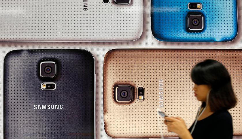 A commuter uses her mobile phone as she walks past a Samsung Galaxy mobile phone advertisement in Singapore