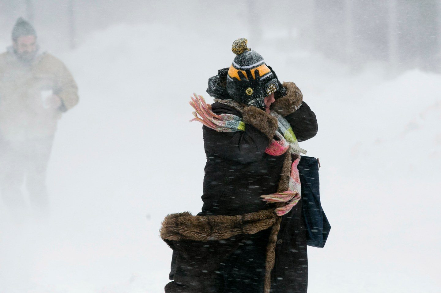 A woman holds onto her hat against the wind during a snow storm in Boston