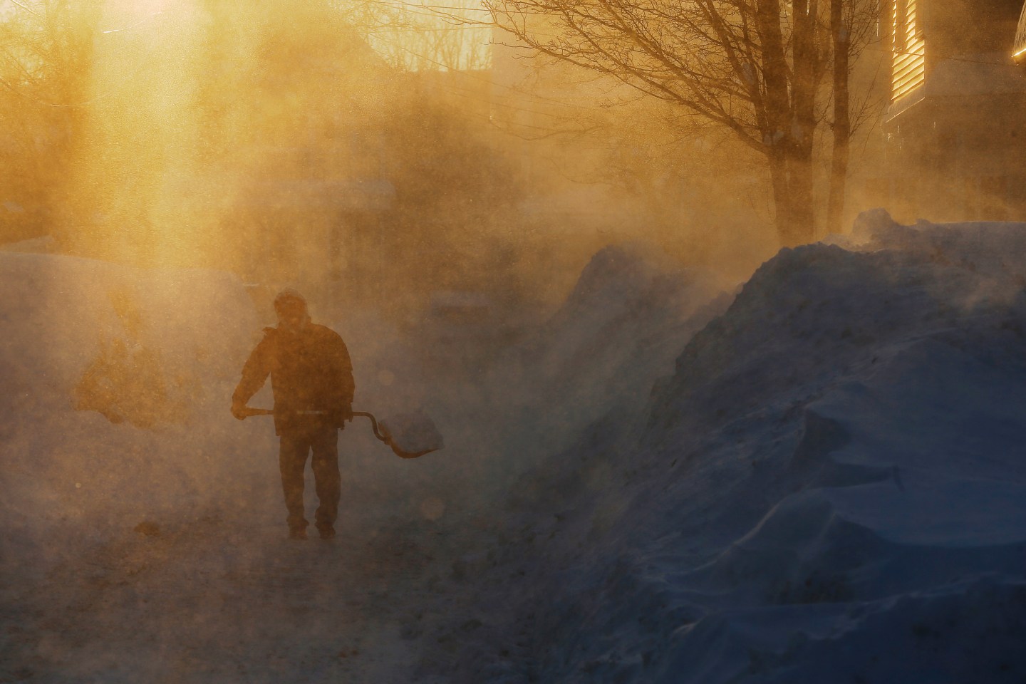 Wind blown snow swirls around a man shoveling snow following a winter storm in Medford