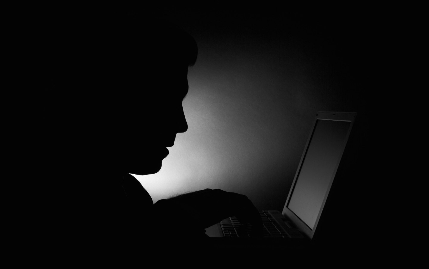 a silhouette of an adult male using a computer laptop. Black and white. Focus on silhouette man face.