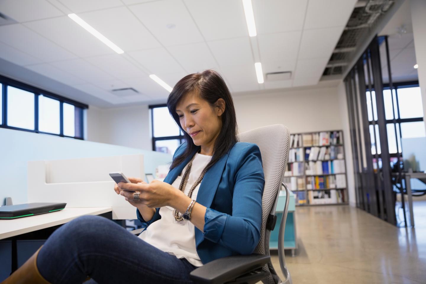 Businesswoman texting on cell phone at office desk