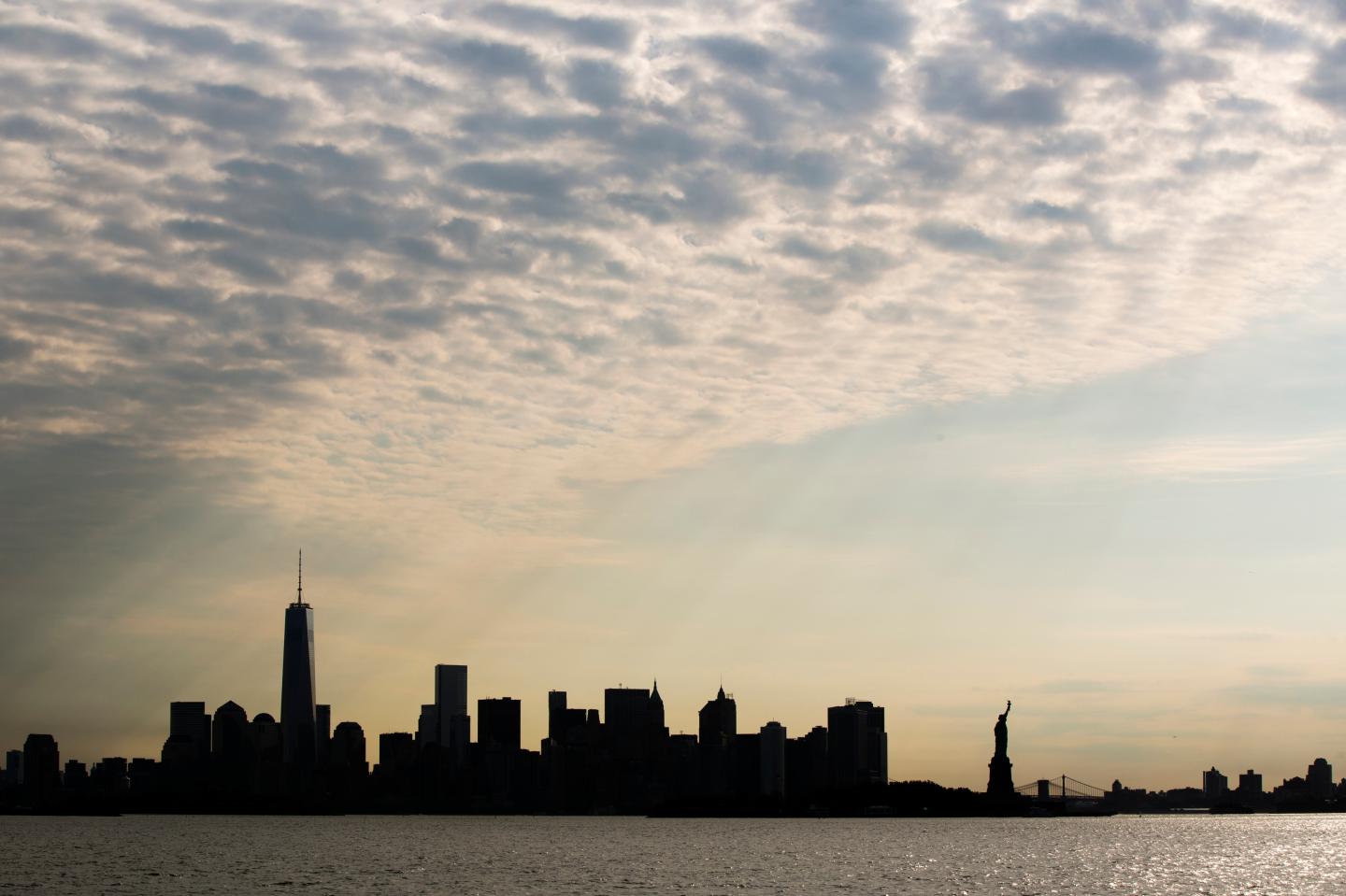 The sun rises behind the Statue of Liberty and the skyline of lower Manhattan in New York