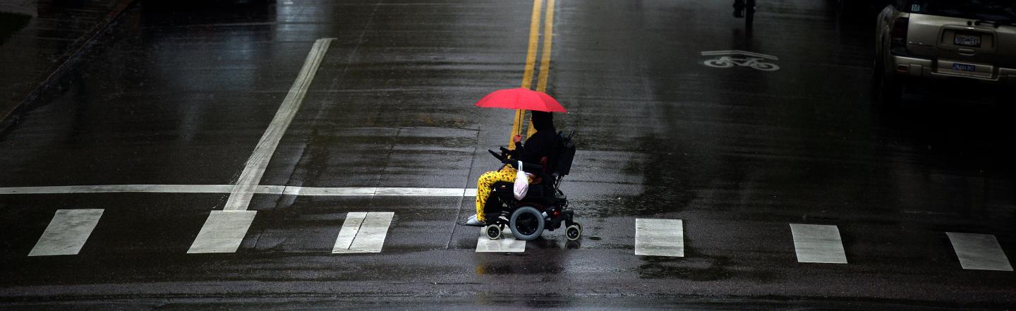 A person in a wheelchair has a red umbrella for protection as they cross Sherman Street at Colfax Ave across from the state capitol  in Denver on a rainy Tuesday.