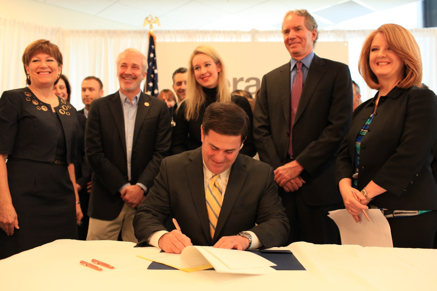 The photo was taken on April 6, 2015, at Theranos's lab facility at SkySong Center, in Scottsdale, Arizona. It shows Arizona Governor Doug Ducey signing into law a bill legalizing direct consumer ordering of any lab test. Behind him is Elizabeth Holmes, founder and CEO of Theranos. At far right is Rep. Heather Carter, of Cave Creek, Arizona, who sponsored the bill. 