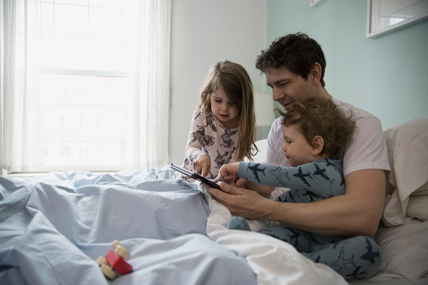 Father and children using digital tablet in bed