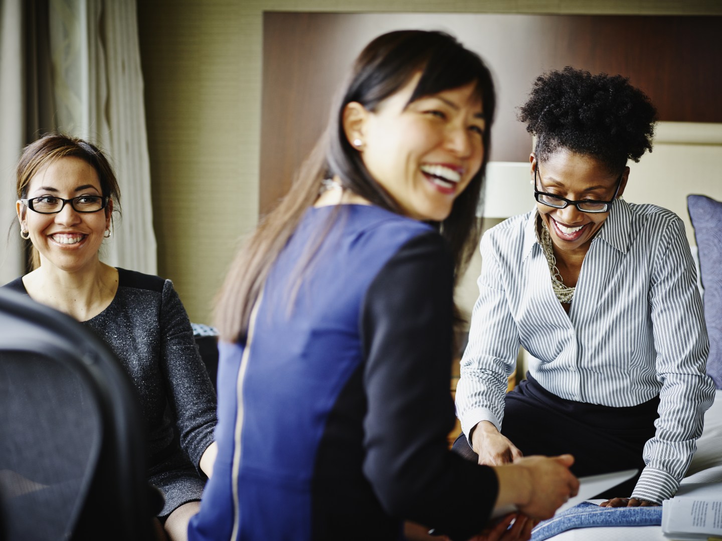 Three smiling businesswomen working in hotel suite