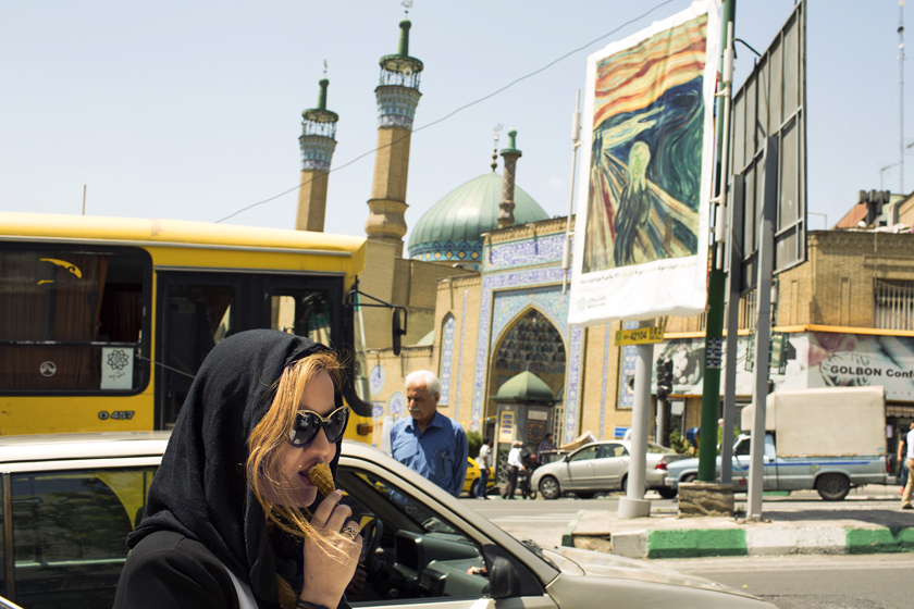 A pedestrian eats ice-cream at in Kaj Square near a billboard displaying a copy of Edvard Munch's "The Scream" painting in Tehran, Iran.