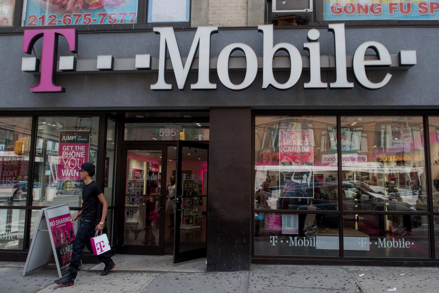 Pedestrians stroll by a A T-Mobile branch on the corner of West 17th Street and 6th Avenue in Manhattan, New York, U.S., on Sunday, July 26, 2015. T-Mobile will be announcing their earnings this week. Photographer: Craig Warga/Bloomberg *** Local Caption ***