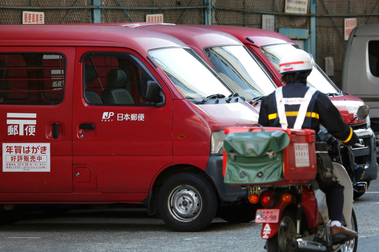 Japan Post vans sit parked while an employee drives a motorcycle into the company's branch in Tokyo, Japan