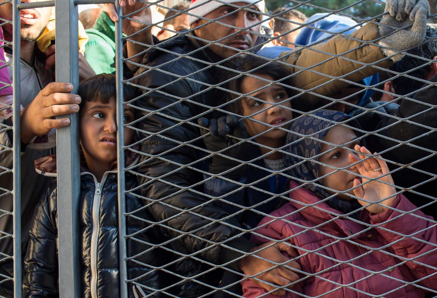 Migrants stand behind a gate as they wait to board buses inside a registration camp in Opatovac
