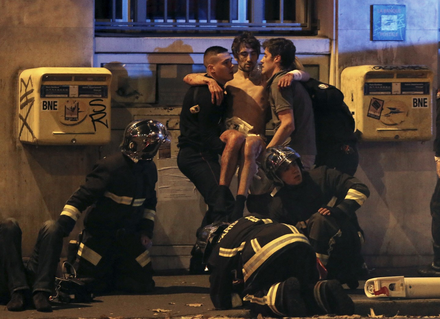 French fire brigade members aid an injured individual near the Bataclan concert hall following fatal shootings in Paris