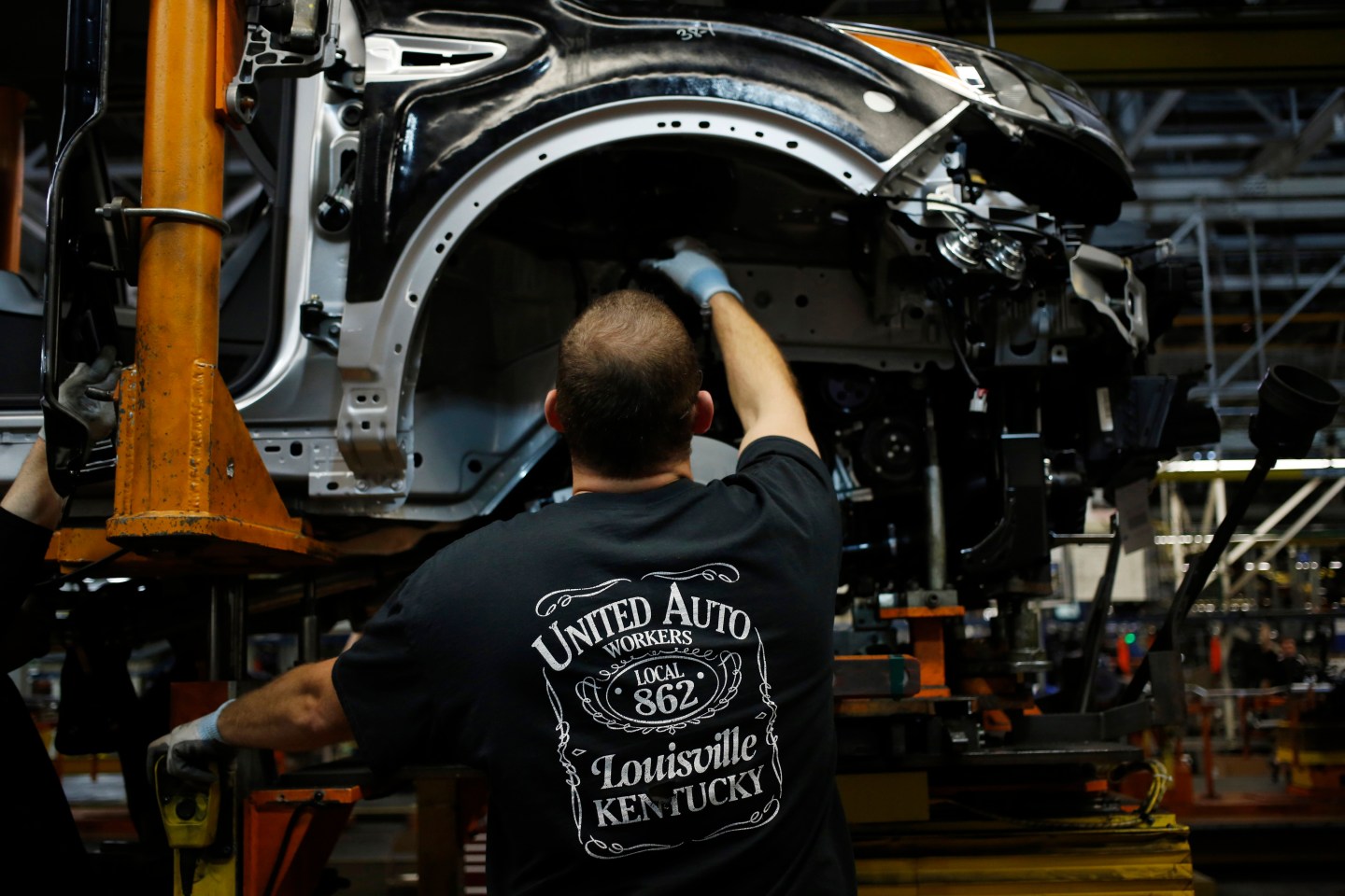 An assembly worker wearing a United Auto Workers (UAW) T-shirt works in the wheel well of a Ford Escape sports utility vehicle at the Ford Motor Co. Louisville Assembly Plant in Louisville, Kentucky, U.S. on Tuesday, April 28, 2015. Photographer : Luke Sharrett / Bloomberg