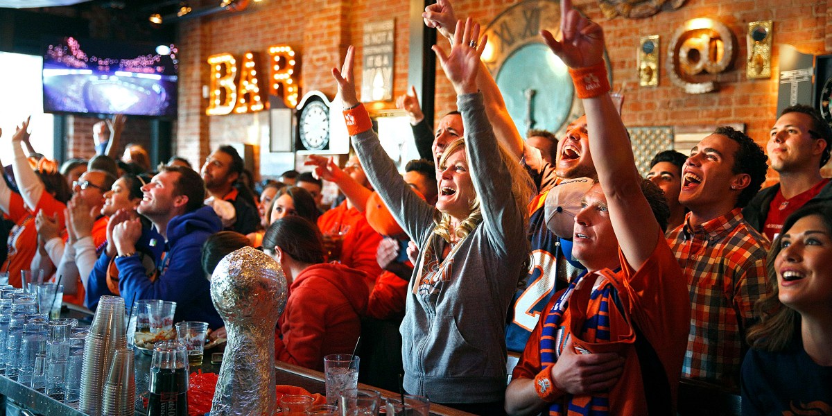 переполненный спортивный бар с большим экраном и болельщиками