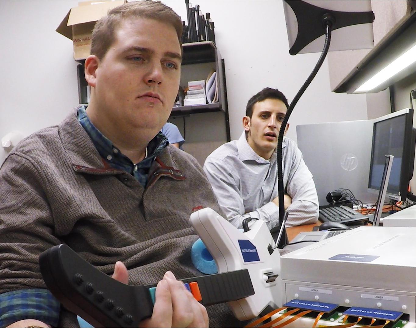 Nick Annetta, right, of Battelle, watches as Ian Burkhart, 24, plays a guitar video game using his paralyzed hand. A computer chip in Burkhart`s brain reads his thoughts, decodes them, then sends signals to a sleeve on his arm, that allows him to move his hand.