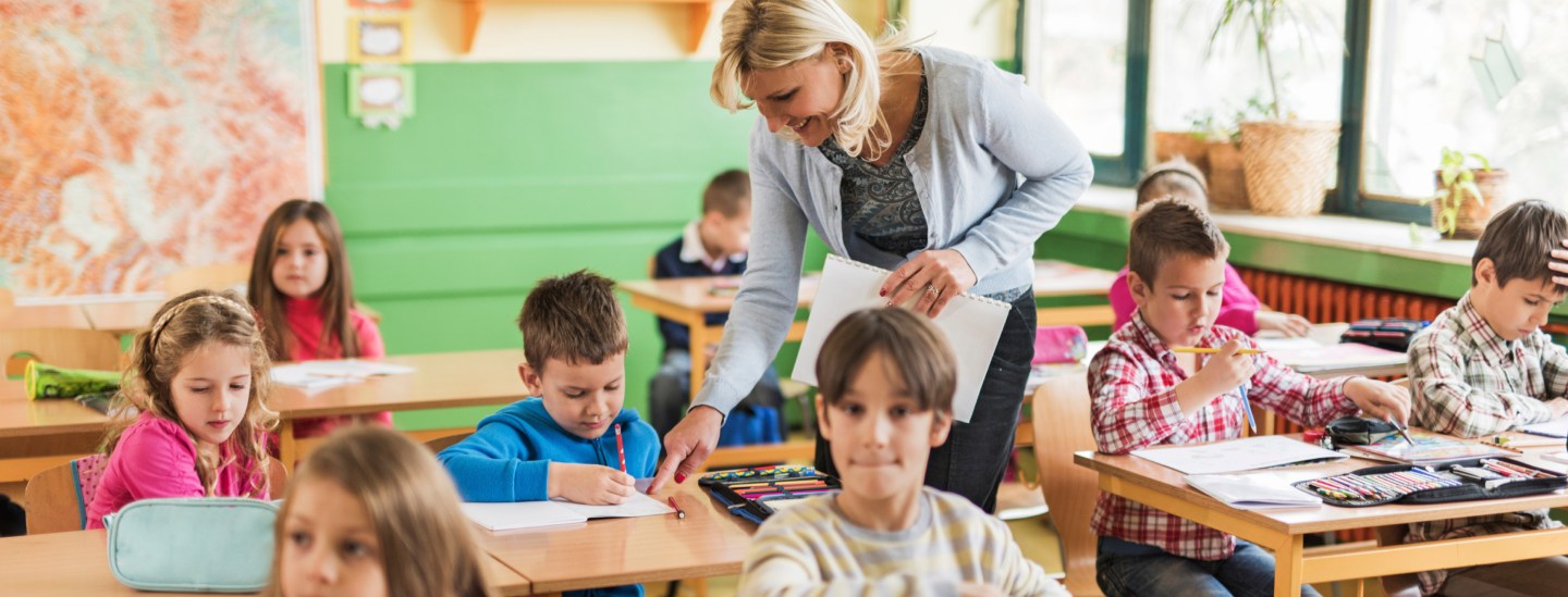 Happy female teacher assisting elementary students in the classroom.