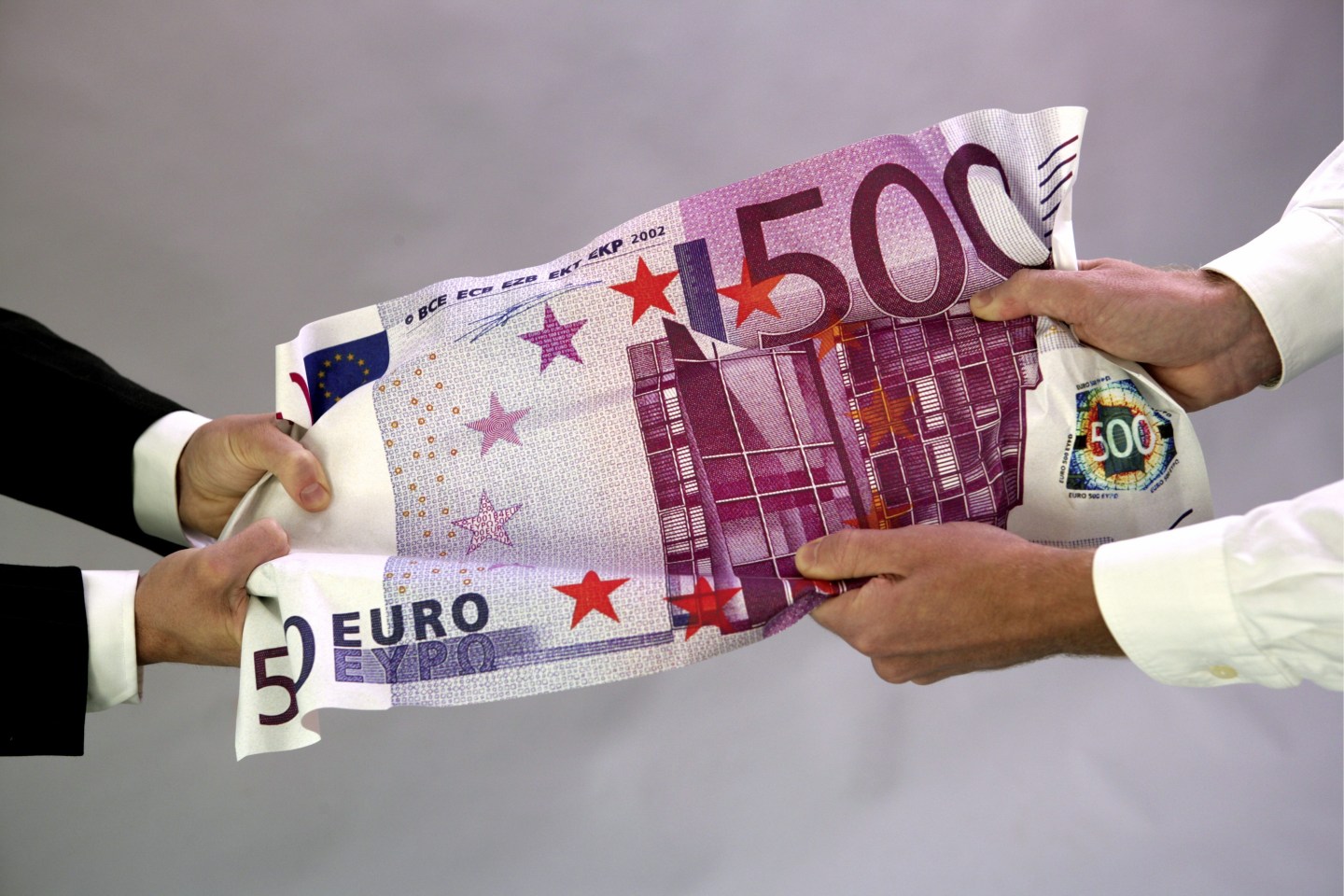 Hands pulling on 500 Euro banknote.