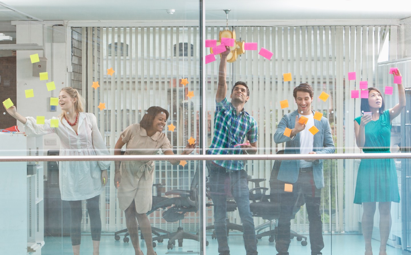 Excited business people with arms raised at window covered in adhesive notes