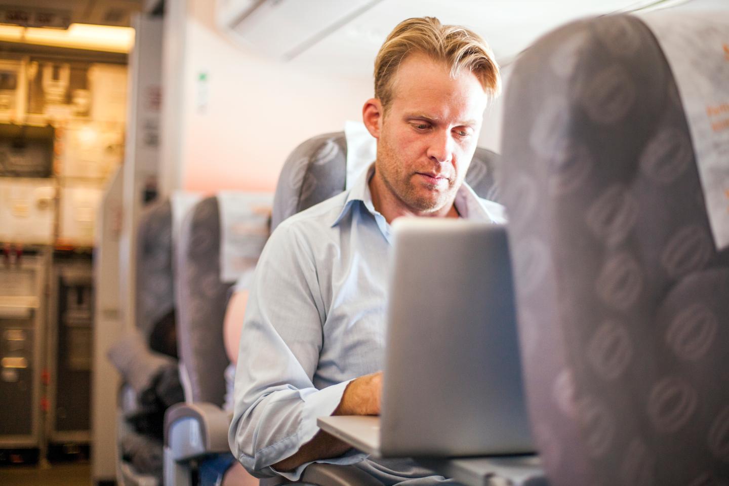 A businessman working on a lap top computer in an airplane.