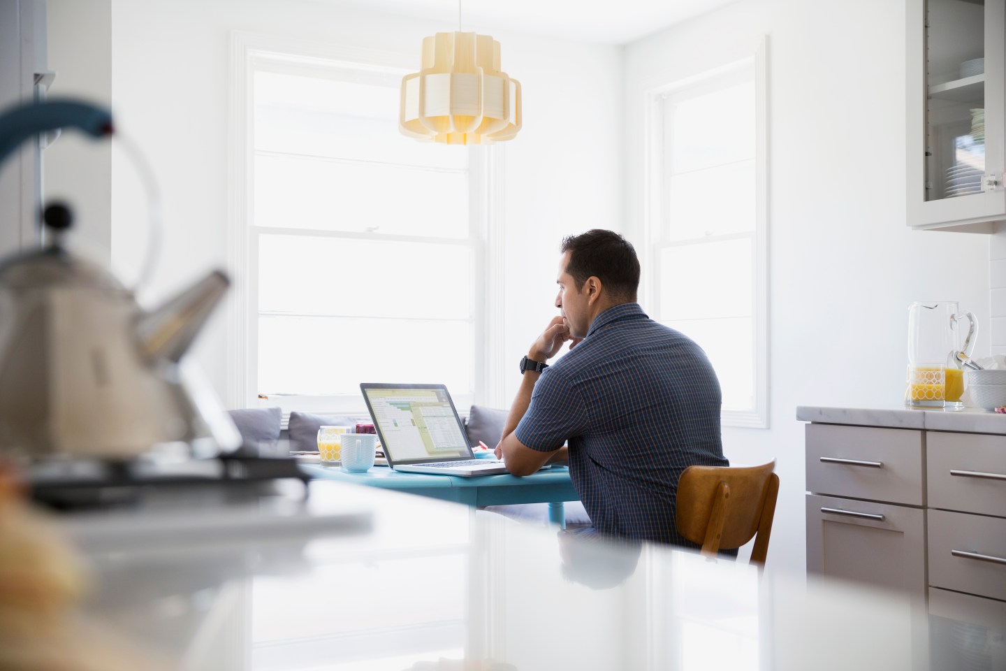 Serious brunette man using laptop at kitchen table