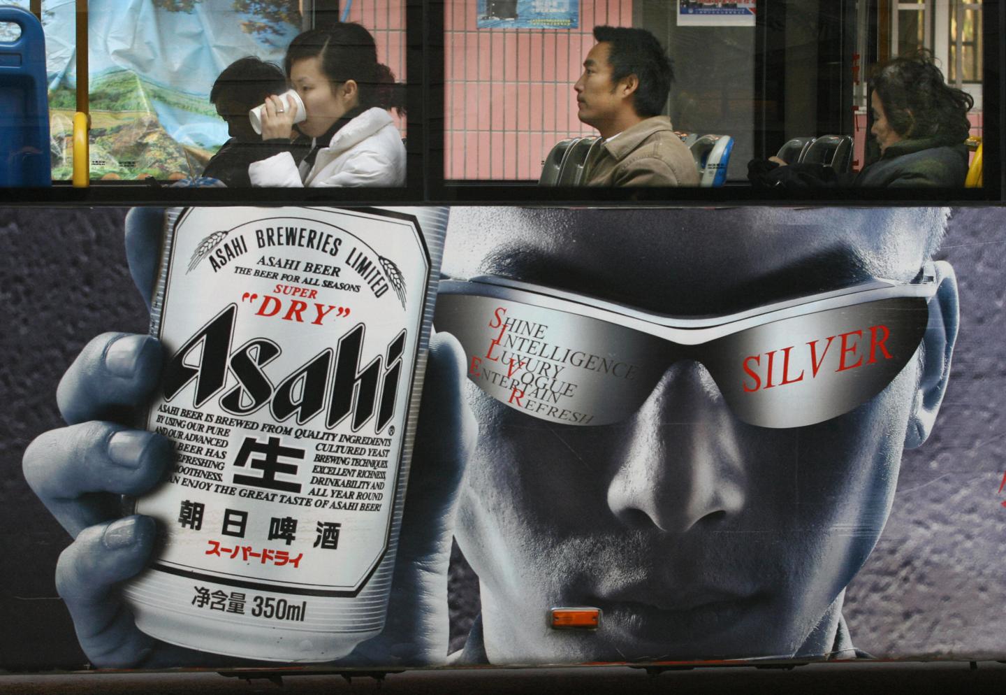 Bus passengers sit above an ad for Asahi