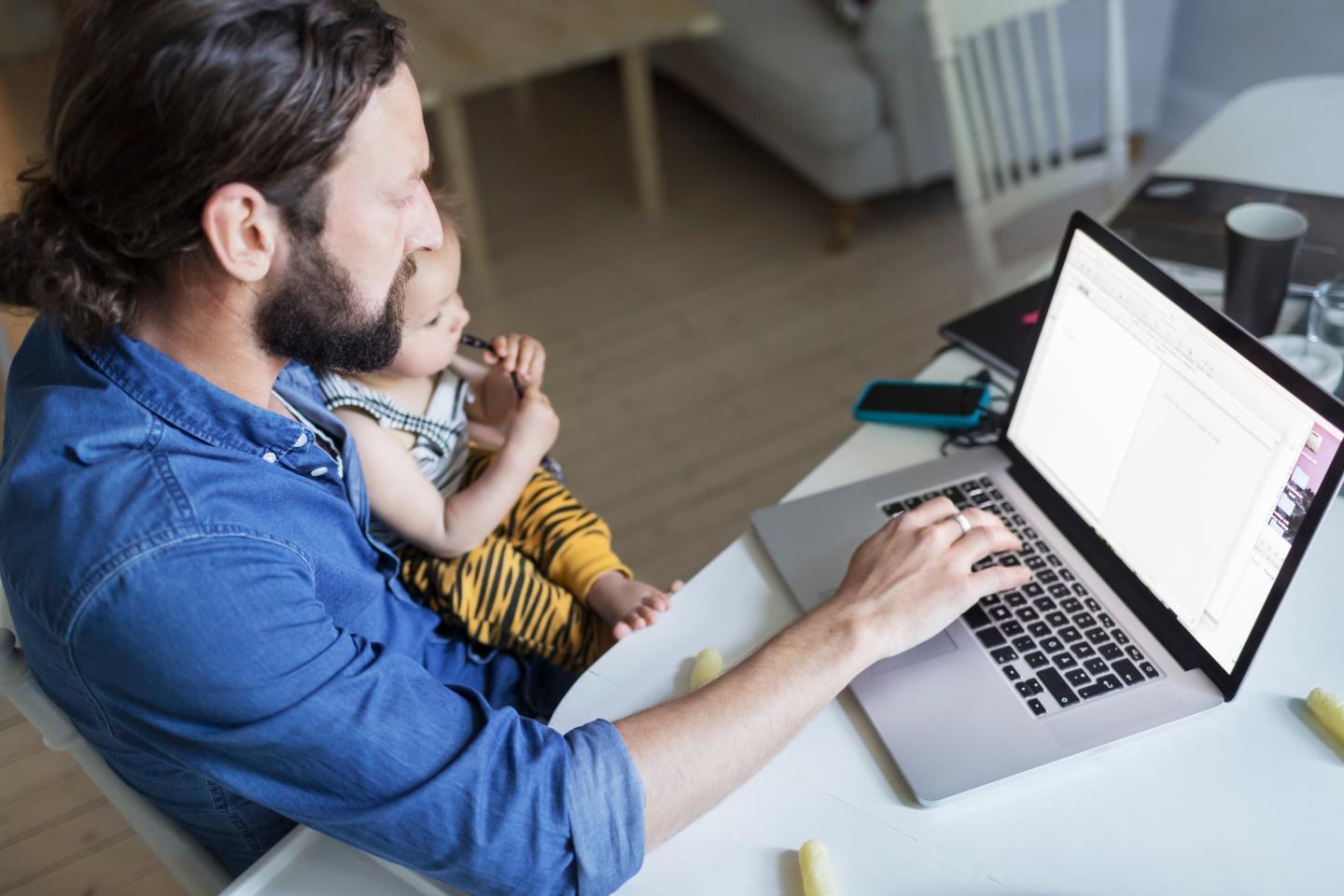 High angle view of mid adult man with baby boys working on laptop at home