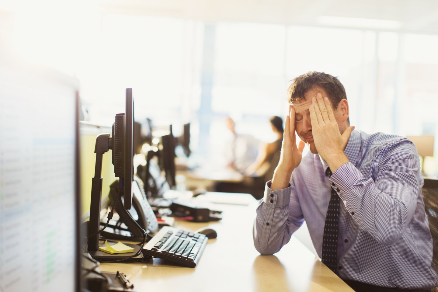 Stressed businessman with head in hands at office desk