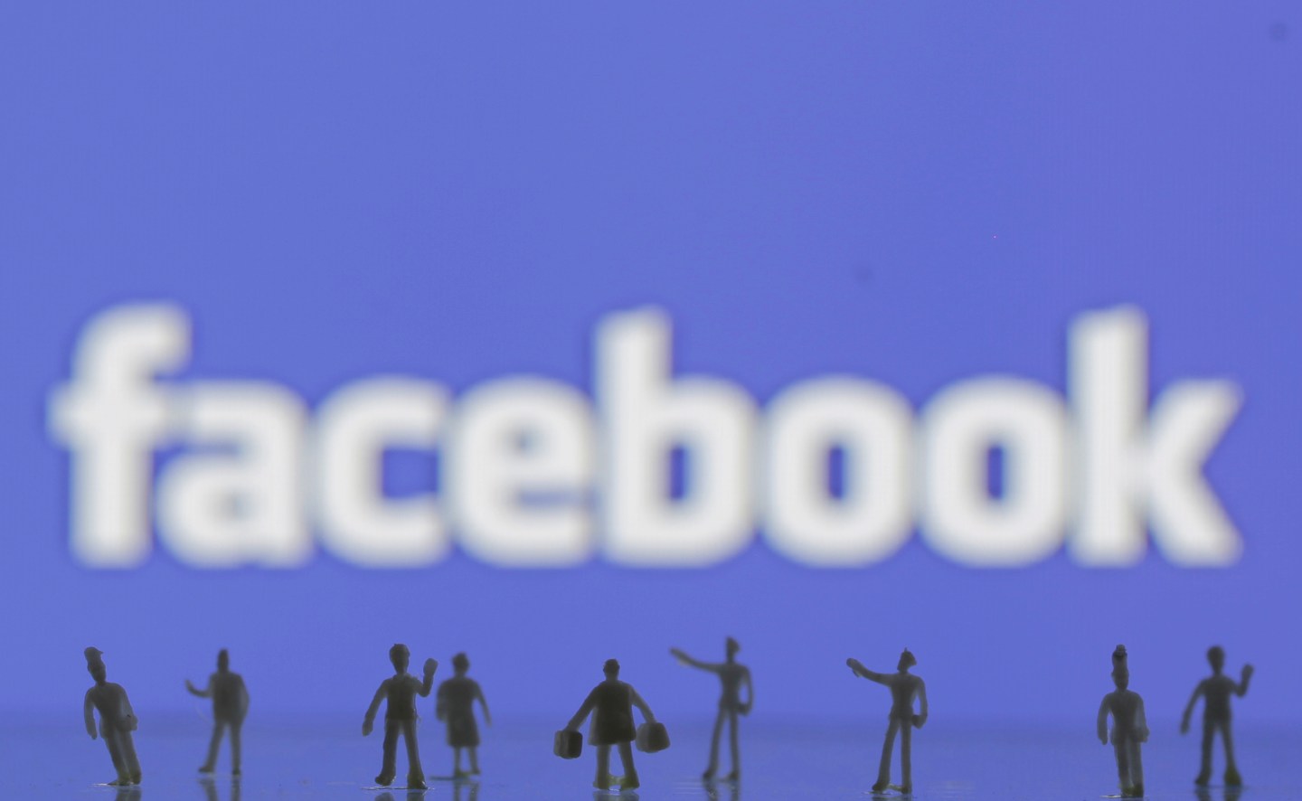 Photo illustration of 3D-printed models of people in front of a Facebook logo