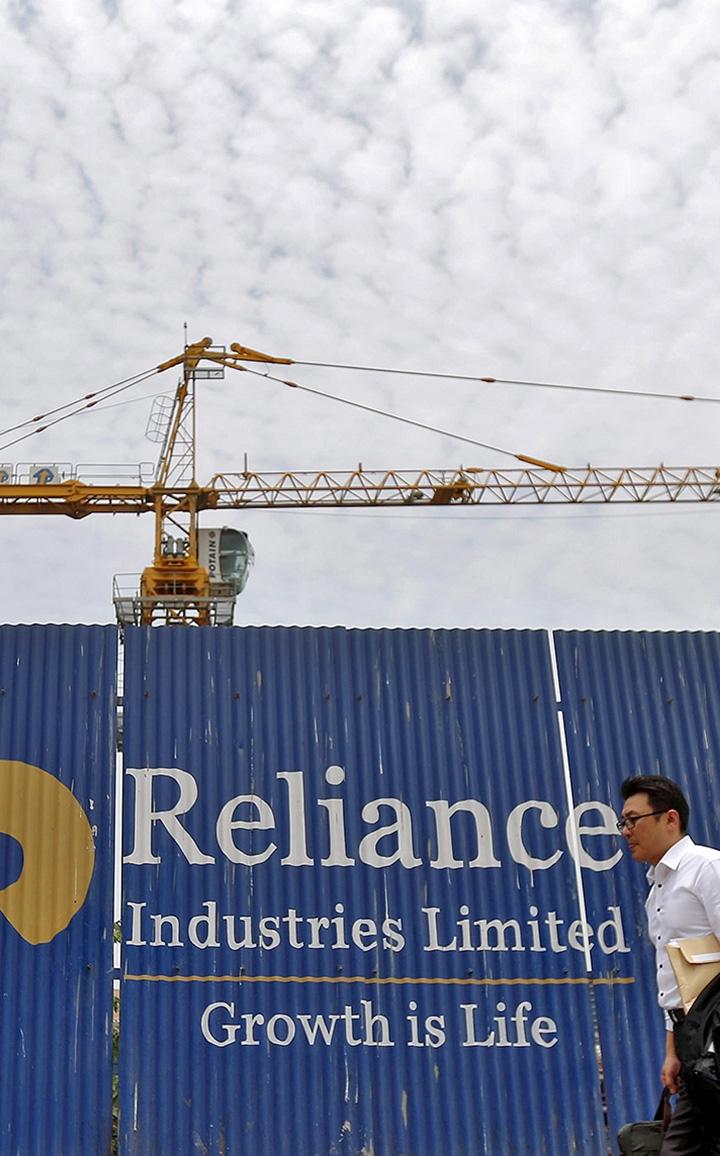 A man walks past an advertisement of Reliance Industries Limited at a construction site in Mumbai