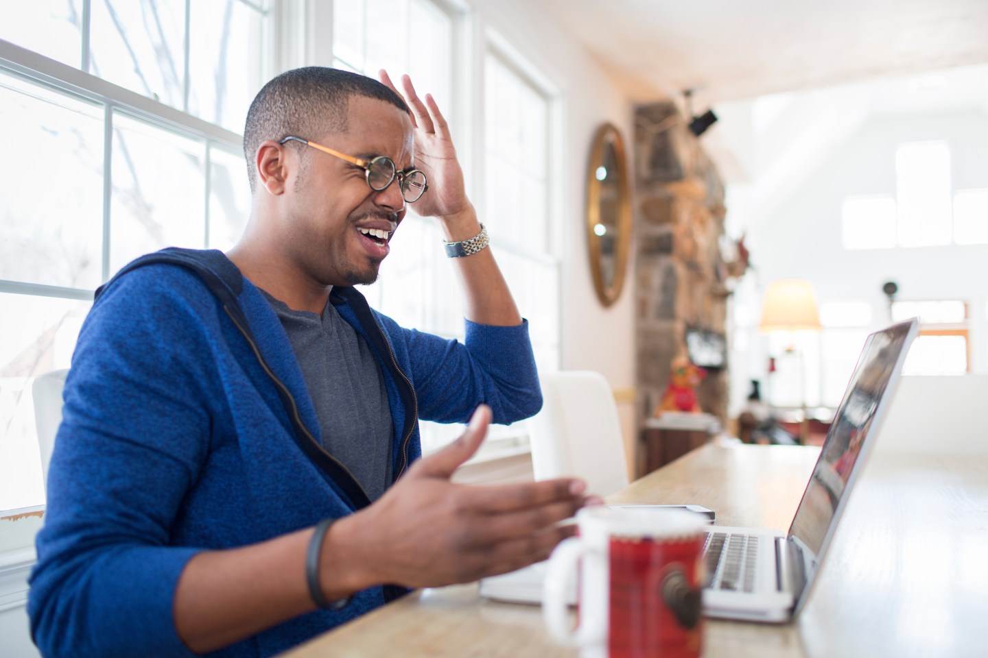 Mid adult man with hands raised in disbelief using laptop at kitchen counter