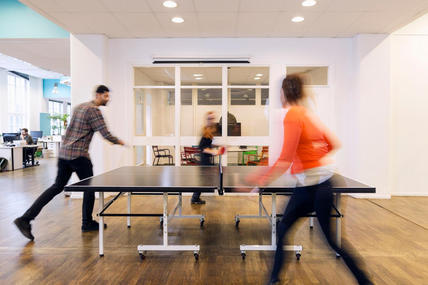 Blurred motion of business people playing table tennis in creative office